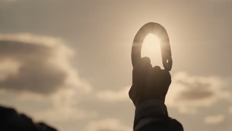 Hand-of-a-man-with-a-horseshoe-against-the-sky-and-the-sun