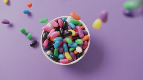 Video-of-close-up-of-multi-coloured-sweets-falling-into-bowl-over-purple-background