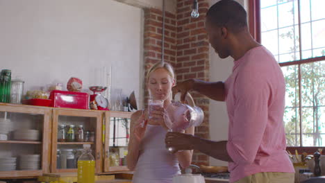 pareja de raza mixta vertiendo batidos caseros en la cocina, filmado en r3d