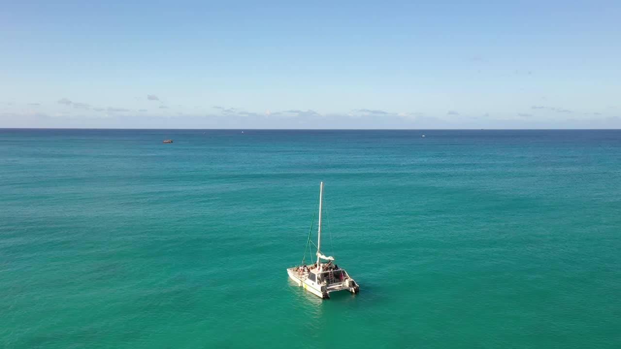 Drone video of a catamaran sailing across turquoise ocean near Waikiki Beach, Oahu, Hawaii. A serene aerial moment capturing island leisure, nautical elegance, and the vast beauty of open water