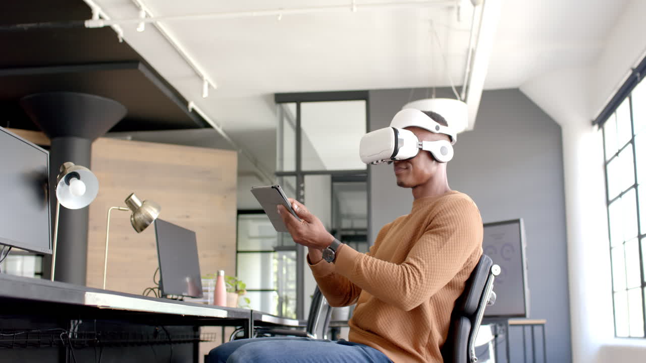 Using VR headset, African American man interacting with tablet in modern office workspace