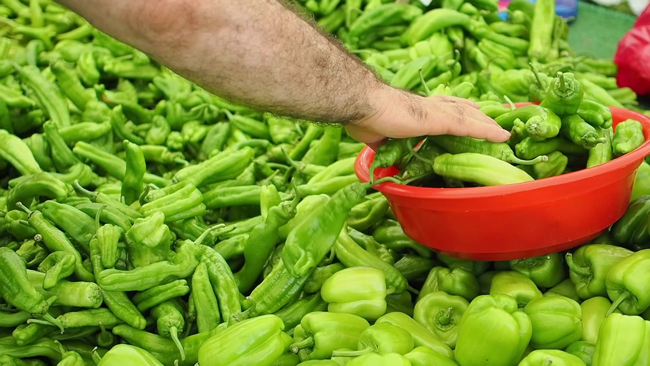 Person Sorting Fresh Green Peppers at a Market Stall