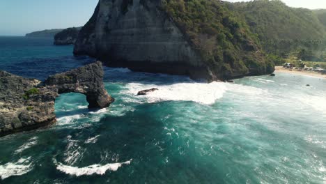 natural rock arch of nusa batupadasan island and huge cliffs coast of nusa penida, bali, indonesia - aerial flyover