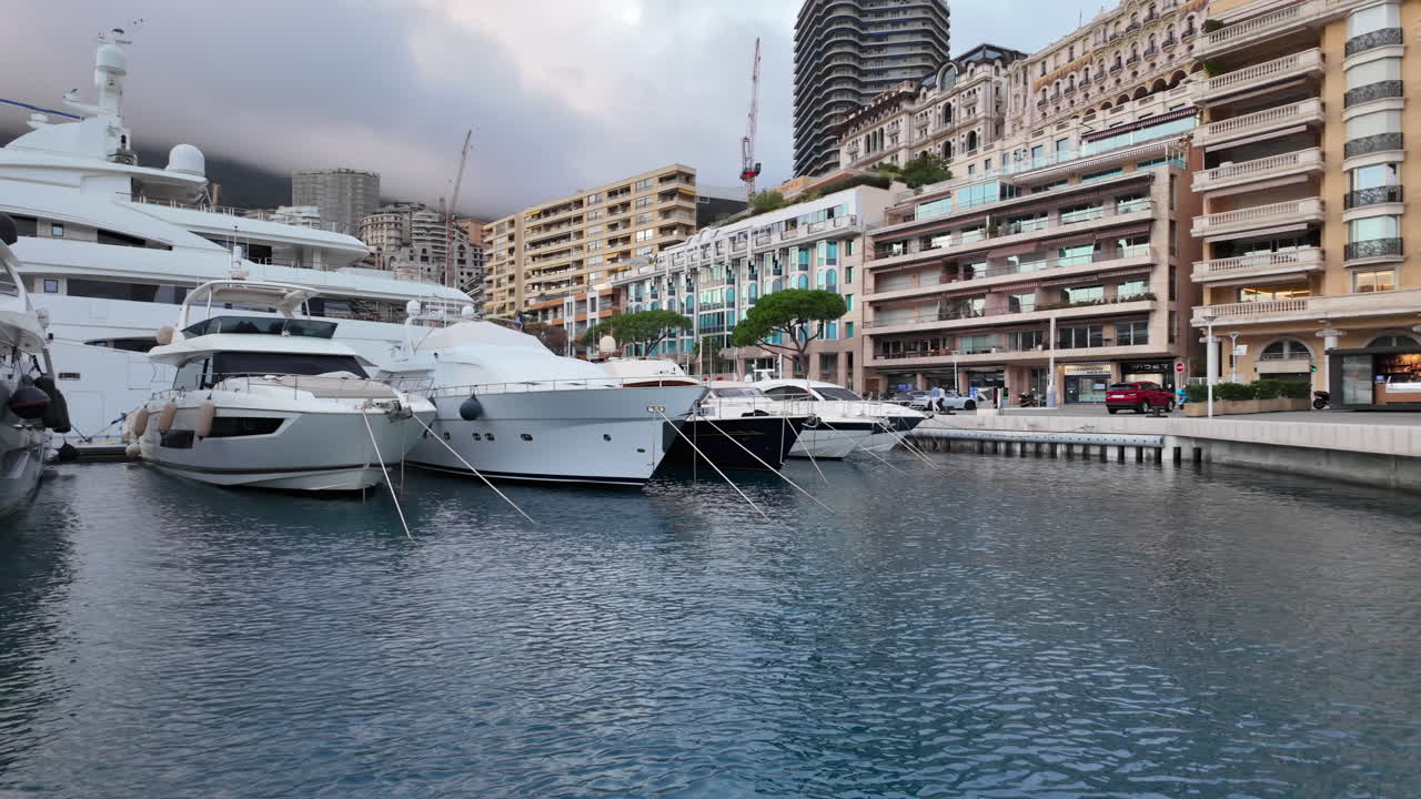 La Condamine, Monaco - July 4, 2025: Row of sleek luxury yachts, docked in Port Hercules with the Monaco cityscape and misty hills in the background