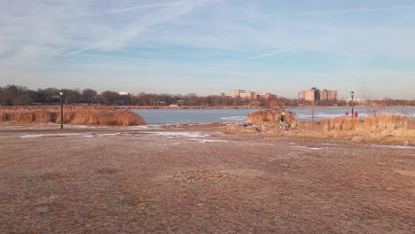 aerial drone footage captures a man running through a park, passing by from a side angle as the camera smoothly transitions toward a frozen lake
