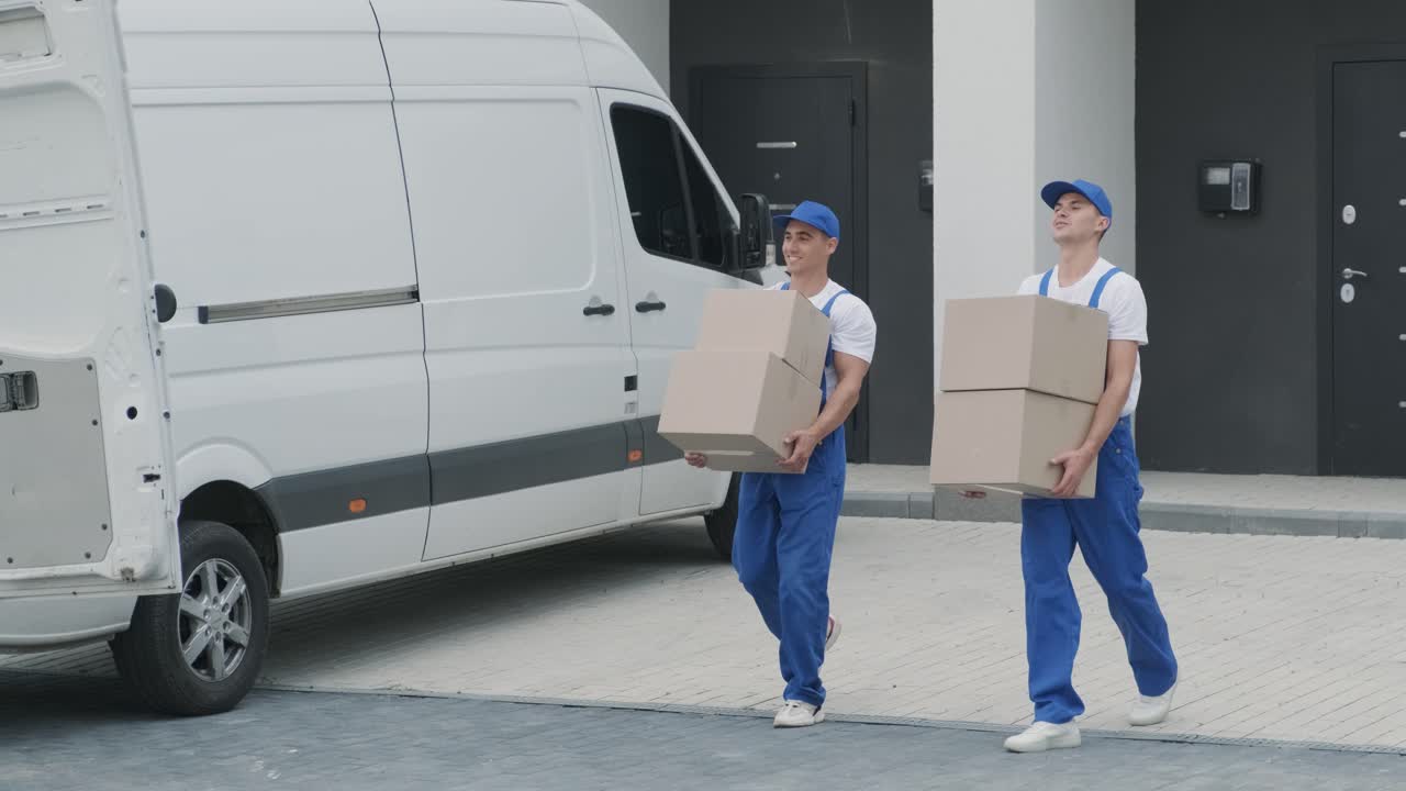 dos jóvenes trabajadores de una compañía de mudanzas están cargando cajas y muebles en un minibus