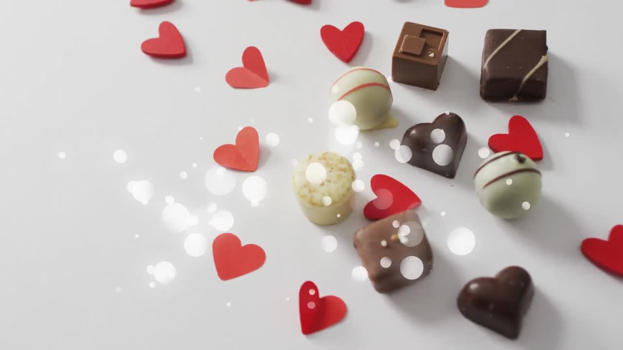 animación de puntos sobre pralines de chocolate y corazones de papel en superficie blanca