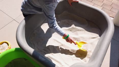 un niño usando una pala amarilla sacando arena en un balde