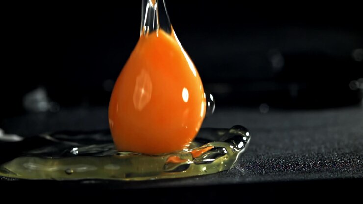 Raw Egg Yolk and White Pouring onto a Black Surface