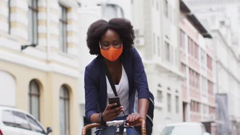 african american woman wearing face mask riding bicycle in street