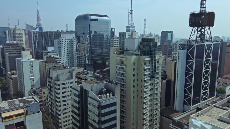 Voo de drone aéreo sobre o centro da cidade de São Paulo, Brasil, edifícios metropolitanos densos e altos no horizonte diurno.