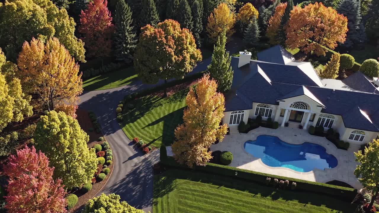 Aerial video view of a luxurious estate surrounded by vibrant autumn trees, showcasing a pool