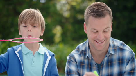 father and son blowing soap bubbles together in sunny park happy little boy having fun dad playing with child playfully enjoying summer 4k