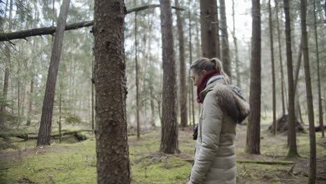 slow motion: young woman walks through the woods while dog plays in the backround