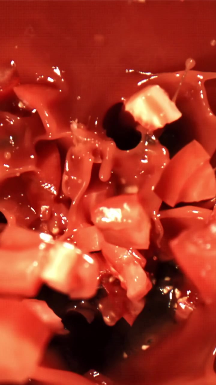 Primo piano al rallentatore di pomodori a cubetti che schizzano in un liquido rosso