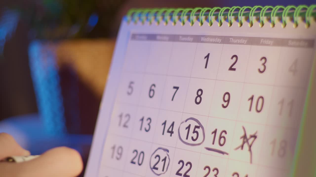 Hånd, der markerer en dato på en skrivebordskalender med en markør.