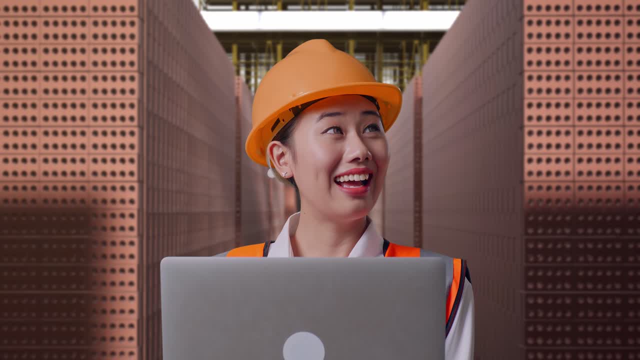 Close Up Of Asian Female Engineer With Safety Helmet Working On A Laptop And Looking Around While Standing With Red Brick Packed in Stacks Are Stored