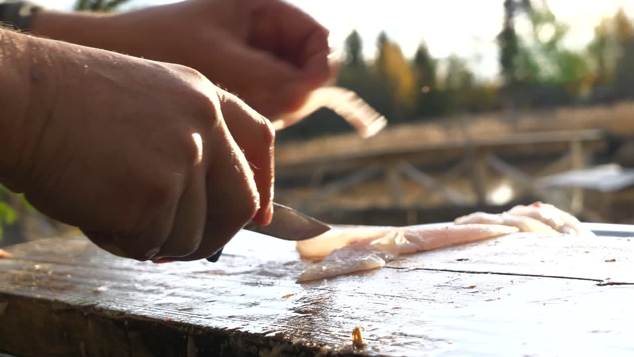 木の板にスズキの切り身を切る男性の手のクローズアップ、日光