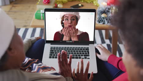 african american mother and daughter using laptop for christmas video call with woman on screen