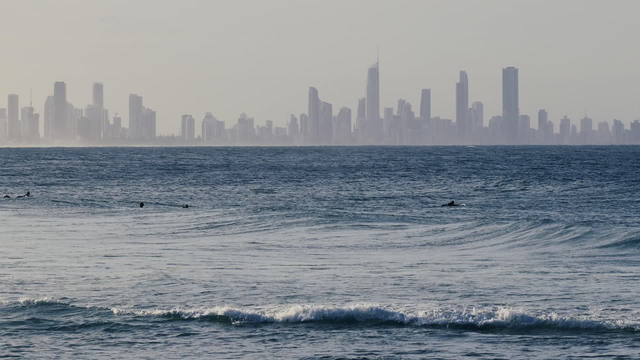 서퍼와 파도가 먼 도시의 스카이라인과 함께