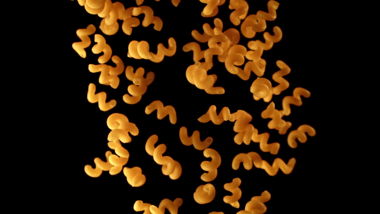 Maccheroni dorati che cadono su sfondo nero