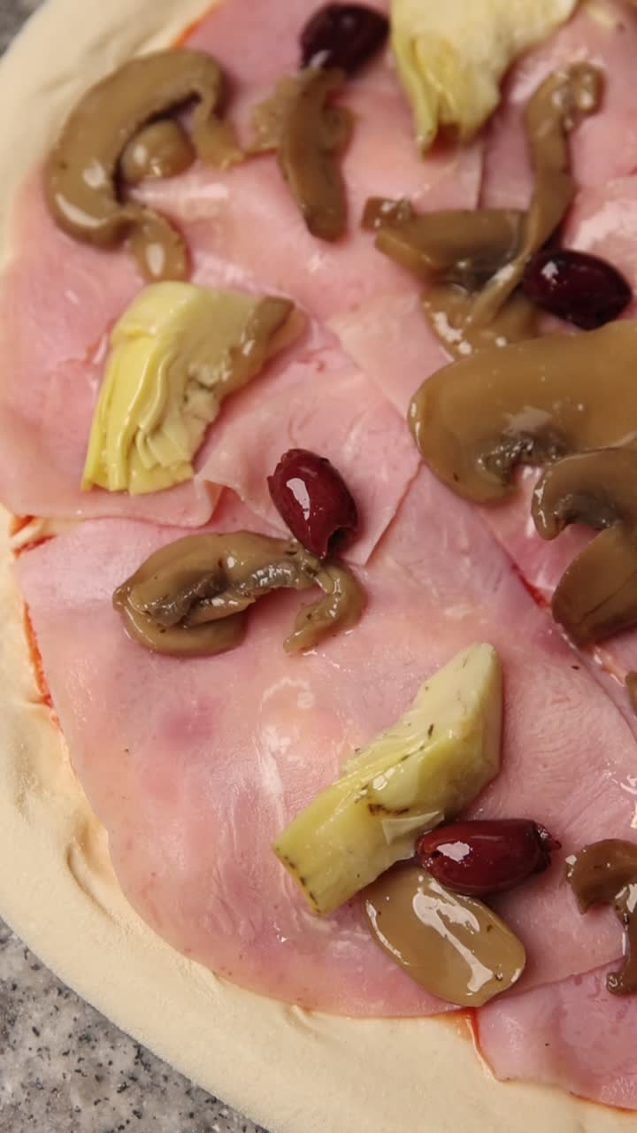 Primo piano di pizza cruda con prosciutto, funghi, carciofi e olive