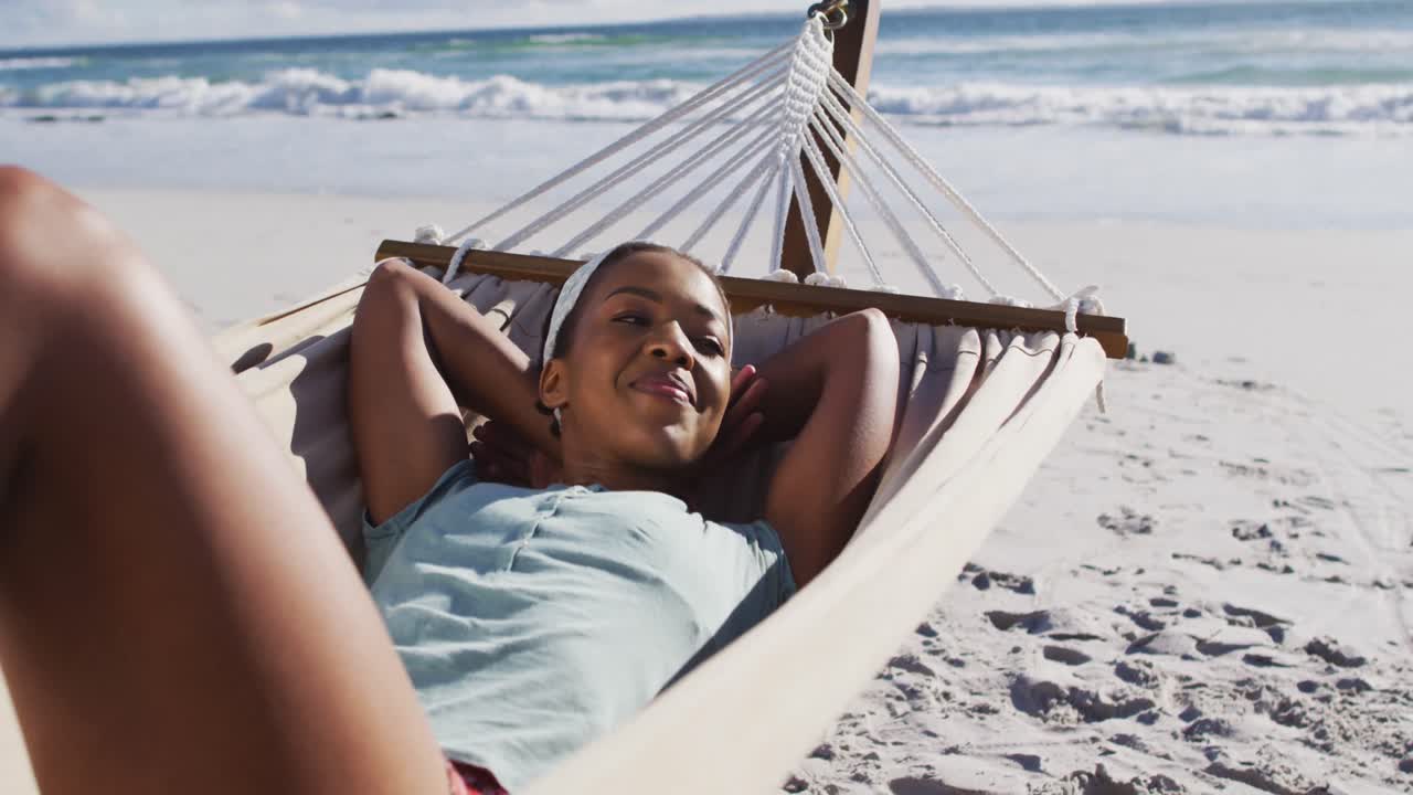 mujer afroamericana sonriendo y acostada en una hamaca en la playa