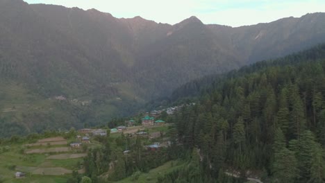 daytime aerial shot of a remote village in a valley on mountain foothills. remote and offbeat with scattered settlement and terrace farms. no human in frame