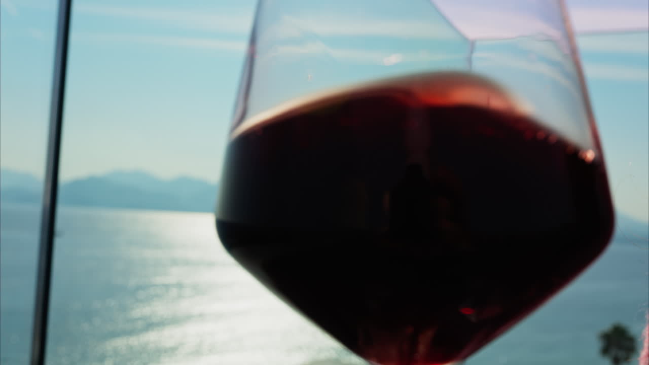 Close up of a woman swirling a glass of red wine on a table at a terrace with a sea view