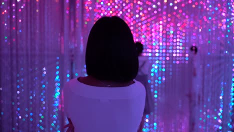 following back of female walking through colorful neon lights at art exhibition