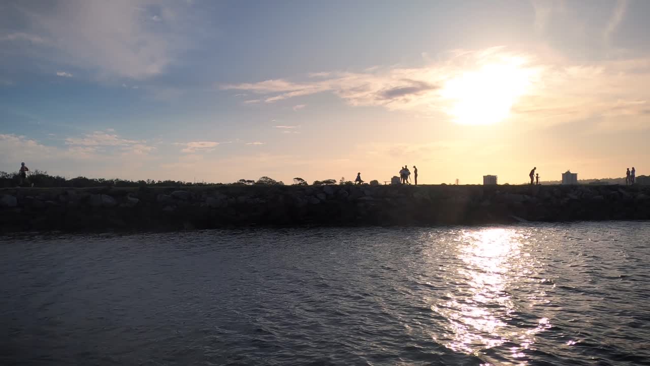 일몰 때 암벽 부두에서 달리고, 걷고, 이야기하는 사람들의 넓은 사진