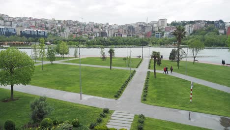 people walking in a city park with a lake and buildings in the background