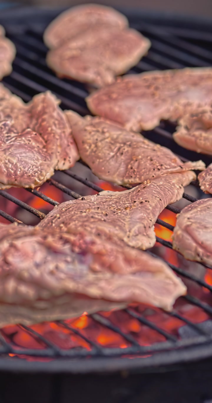 Seasoned chicken meets glowing coals in a tight vertical close-up, capturing the first seconds of charcoal cooking with vivid heat, rich texture, and real homemade appeal.