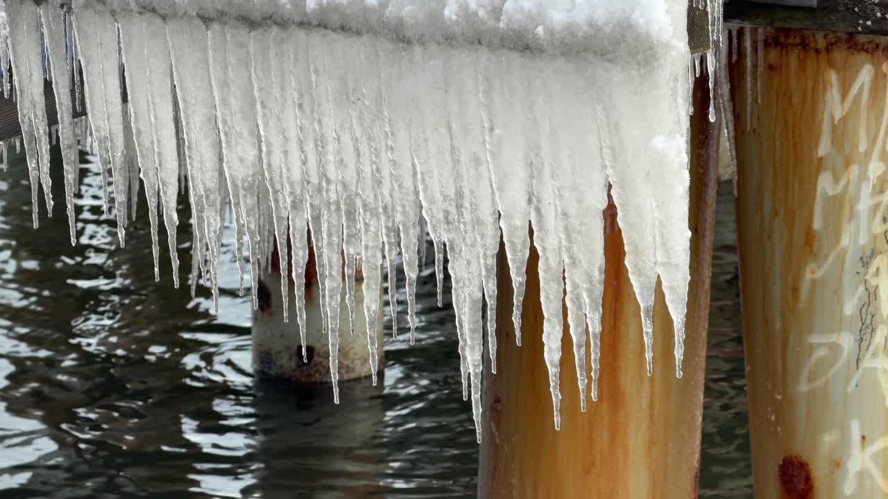Ghiaccioli appesi sotto un molo di legno ghiacciato, scena invernale fredda.