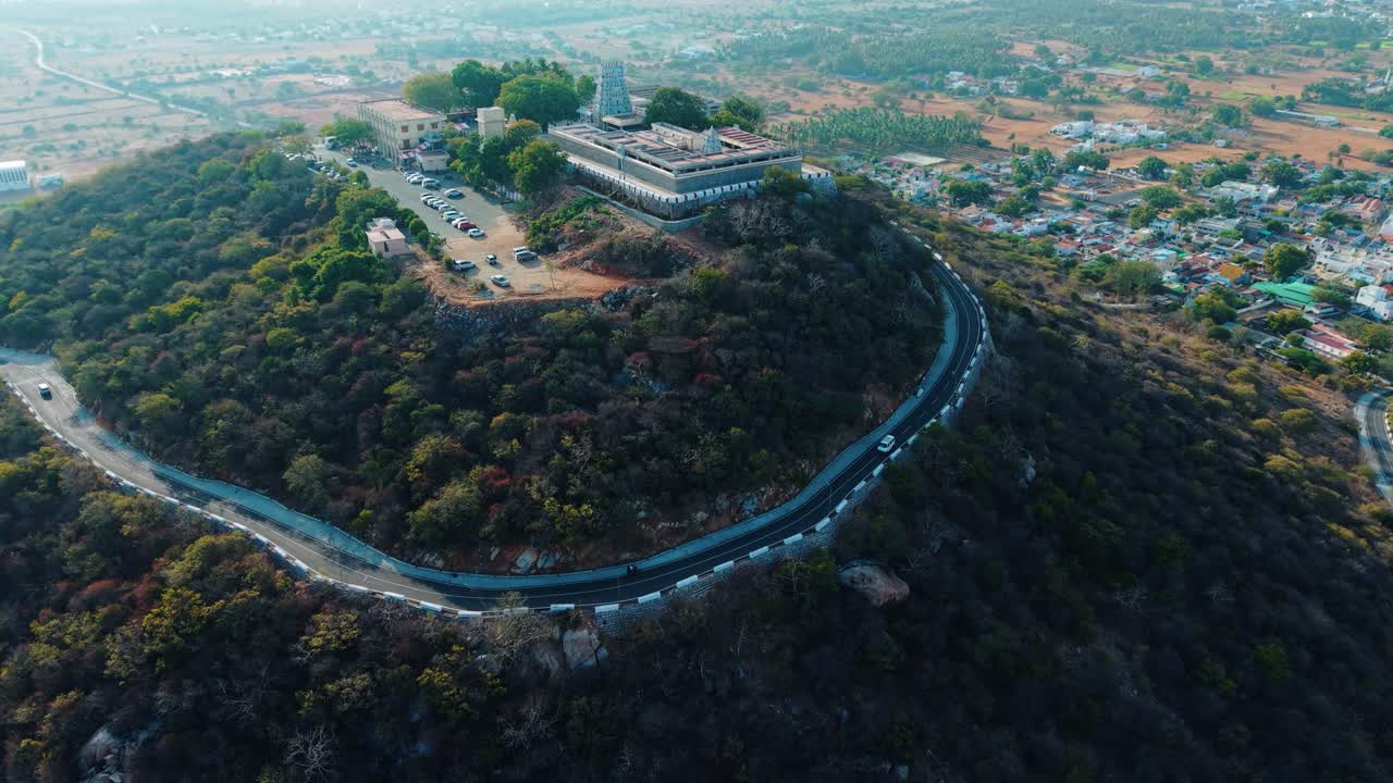 Aerial drone view of Sivanmalai temple majestically seated on a mountain top, overlooking a bustling village at its foothills, symbolizing spiritual devotion and scenic cultural heritage