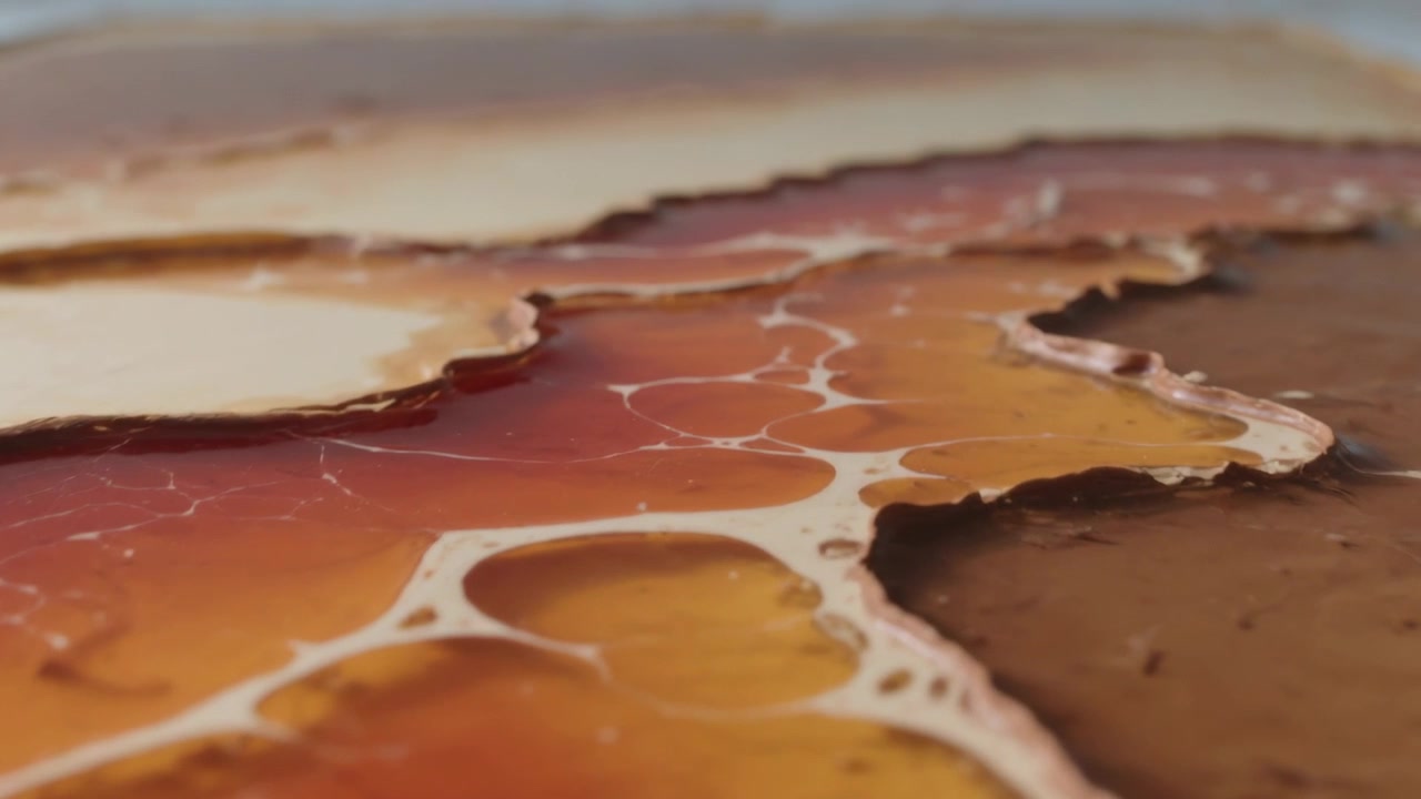 La telecamera si allontana mentre gli strati versati si depositano e si diffondono su un vassoio d'arte, formando venature bianche.