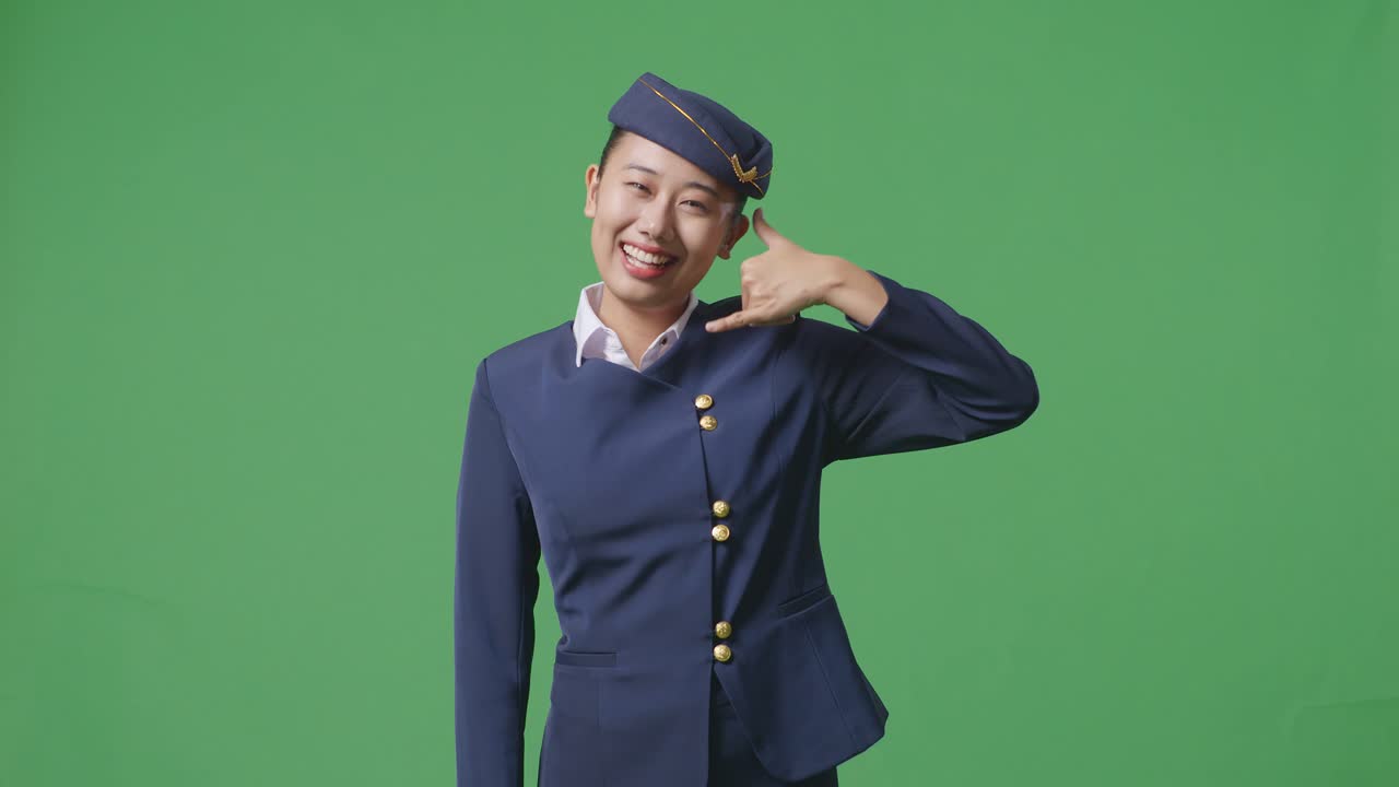 아시아 여성 승무원이 미소 짓고 녹색 스크린 배경 스튜디오에 서있는 동안 카메라에 제스처를 호출합니다.
