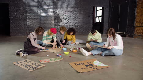 jóvenes activistas ambientales pintando carteles sentados en el suelo