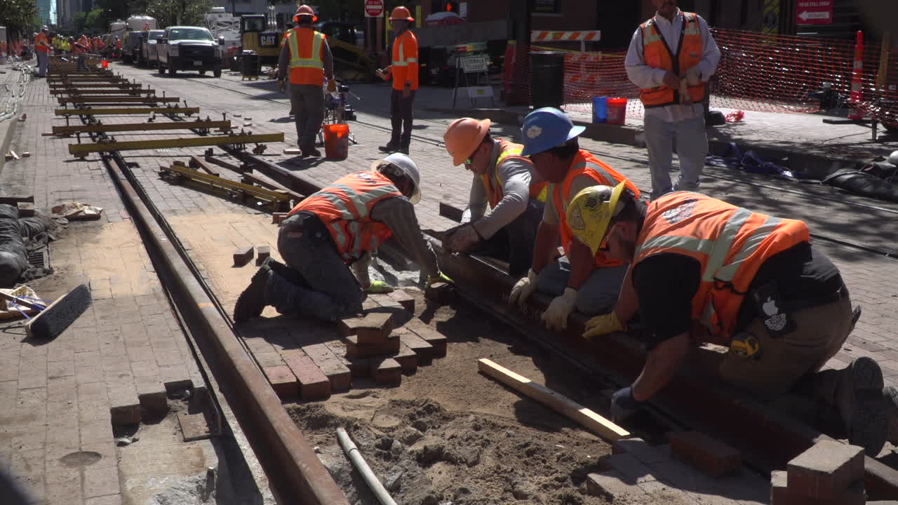 Slow motion video of workers laying new bricks between railroad tracks in a city. They are creating the cobblestone look to the city.