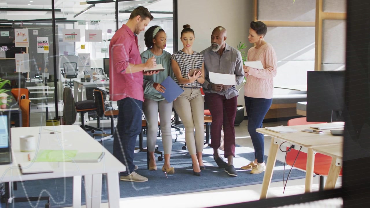 Team of five meeting, left man tapping tablet and causing onscreen charts for business review