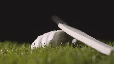 studio cricket still life with close up of ball rolling next to bat and glove lying in grass 1