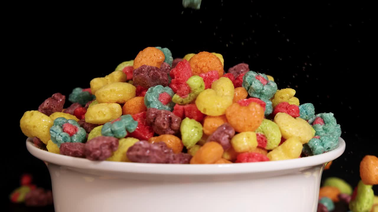 Vibrant cereal pieces cascade into a white bowl against a dark backdrop, creating a dynamic and colorful visual