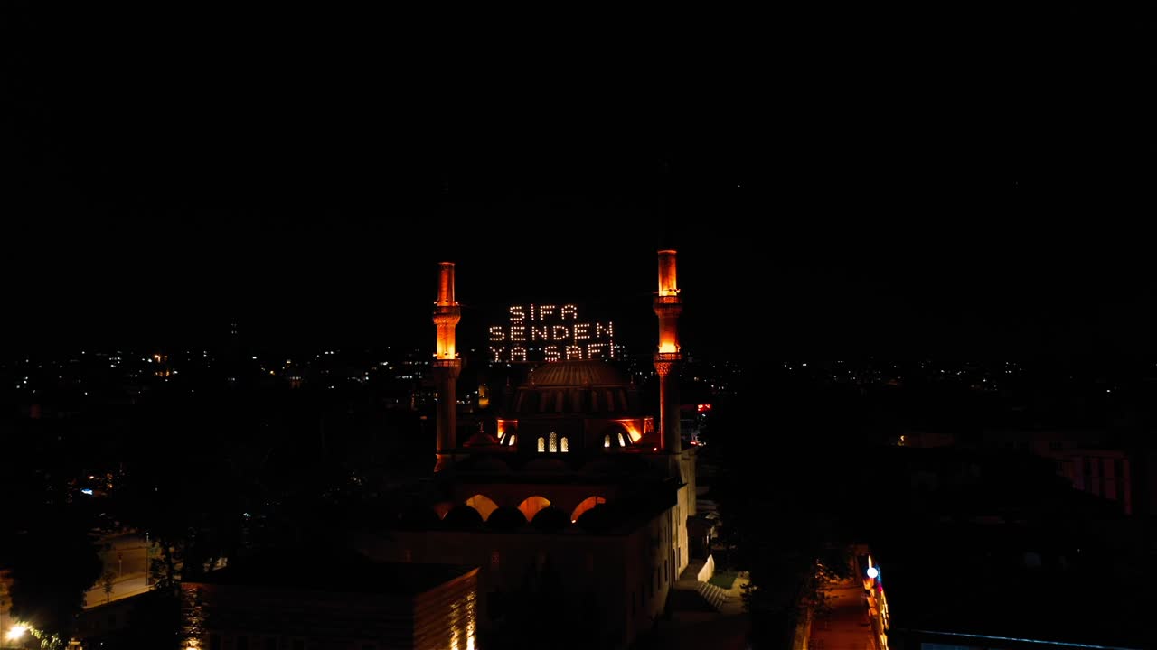 vista aérea nocturna de la mezquita mihrimah sultan. dice "la curación es de dios"