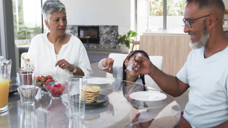 familia biracial disfruta del desayuno, con un niño alcanzando la comida