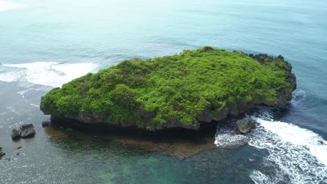 Drone-view-of-huge-coral-rock-with-clusters-of-small-rocks-that-surround-it-and-crushing-by-the-wave