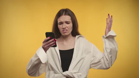 young adult caucasian woman is upset by the news on her smartphone on a bright yellow background