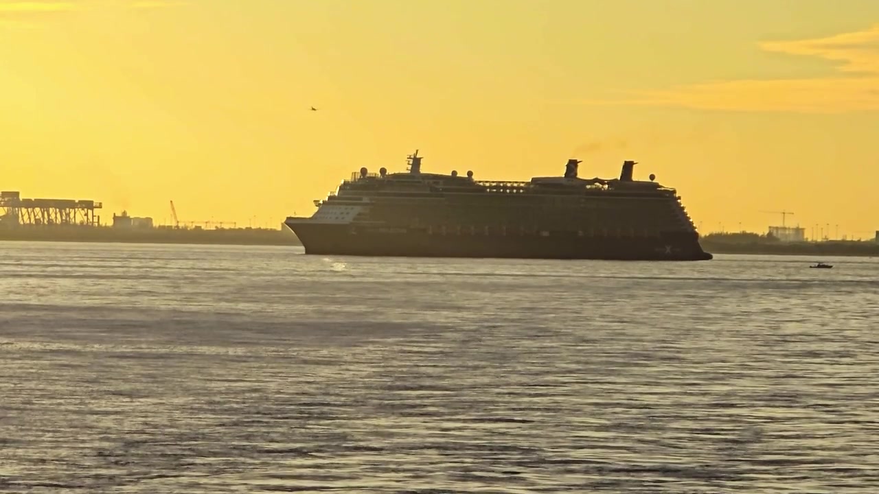Dramatik bir gün batımı gökyüzüne karşı altın rengi sularda seyreden bir Celebrity Cruises gemisinin üst yapısına ve belirgin bacalarına odaklanan detaylı bir yakın çekim.