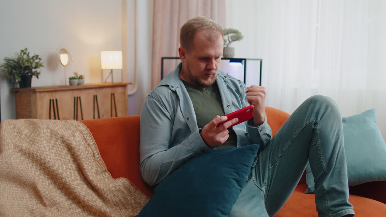 Uomo adulto divertente e preoccupato che gioca a sparatutto online e festeggia la vittoria sul cellulare a casa