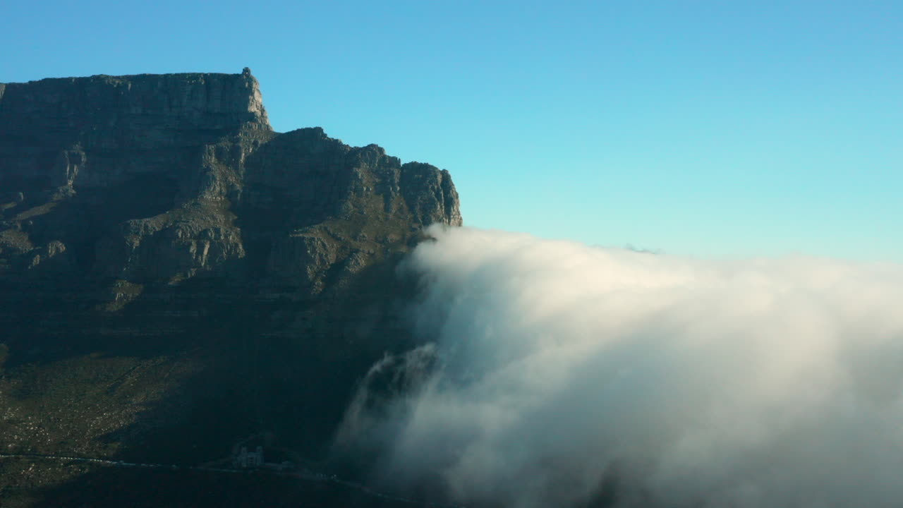 Aerial of Table mountain Table Cloth while clouds come from Camps Bay and evaporate above Cape Town