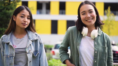 Outdoor-Portrait-Of-Two-Beautiful-Young-Japanese-Girls-Bumping-Fists-While-Smiling-And-Posing-At-Camera-In-The-Street